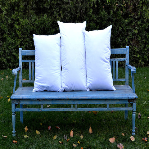 3 white, 180 thread count poly/cotton blend plush pillows stacked beside each other vertically on a blue park bench