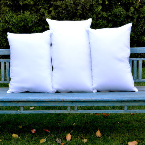 3 white, 180 thread count poly/cotton blend plush pillows stacked beside each other vertically on a blue park bench