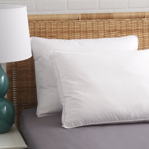 Two PureAssure Allergen Barrier Down Alternative 2" Gusset Pillows leaning a brown whickered headboard.