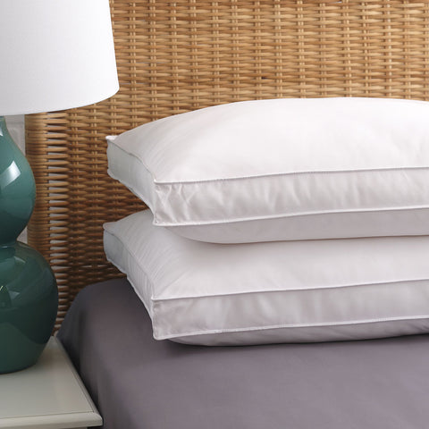Two PureAssure Allergen Barrier Down Alternative 2" Gusset Pillows allowing atop one another flat on the bed. On the side is two white horizontal lines, creating a rectangle that wraps around the ends of the pillow.