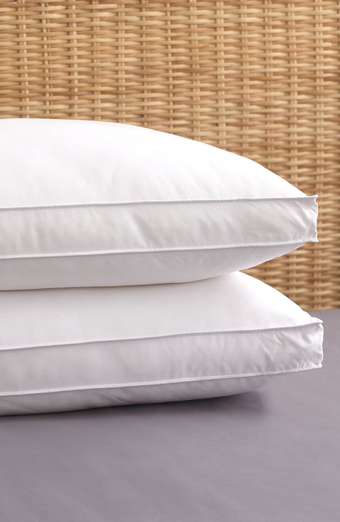 Two PureAssure Allergen Barrier Down Alternative 2" Gusset Pillows allowing atop one another flat on the bed. On the side is two white horizontal lines, creating a rectangle that wraps around the ends of the pillow.