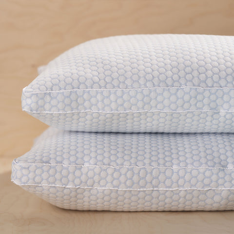 Two CoolMax pillows stacked atop one another. The photo focusing on the left sides of the pillow, getting  aside view of the longer side of the pillows. The pillow features a distinctive white and blue dotted pattern on the pillows.