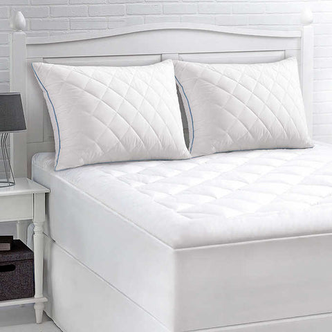 Two pillows with diamond shapes on them and blue stitching along the sides, leaning on the head board beside one another. Crafted with a 300 thread count cotton cover infused with temperature-regulating ClimaRest®, these pillows are also quilted with Suprelle® Cool Night gel fiber for effective heat dissipation. White head board. 