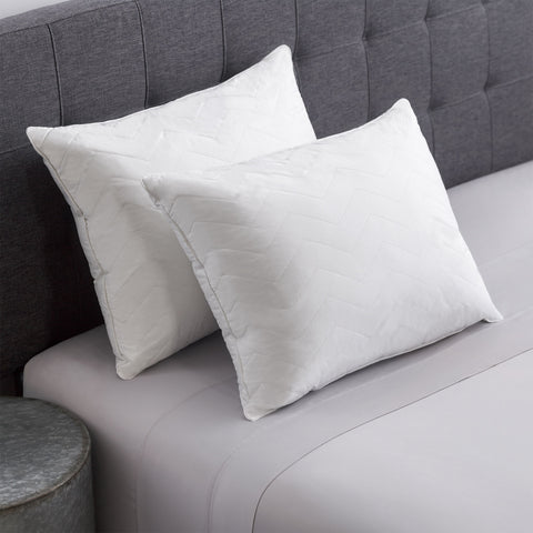 Herringbone Quilted Pillow 2-Pack leaning on a dark grey headboard. The pillows have several horizontal lines running across it, with V shapes alternating facing up and down.