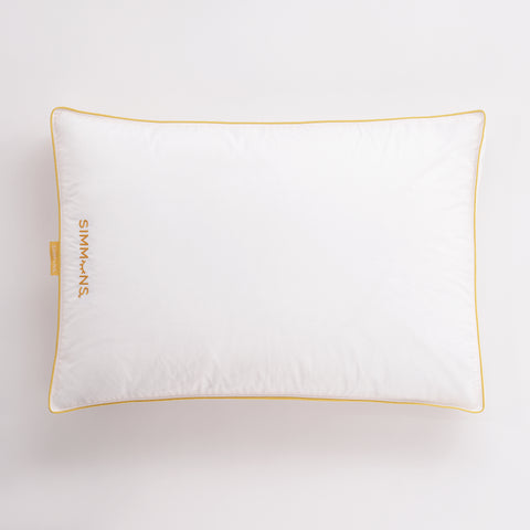 In this image is a up top view of the Simmons Gusset Embroidered Pillow on a white background. The Simmons yellow lining around the ends as always. On the left side of the pillow is a little yellow tag that says Simmons. On the pillow itself also on the left and the text facing the left is the Simmons' logo. The "o" is an image of a closed eye, looks like a parentheses with four eyelashes.