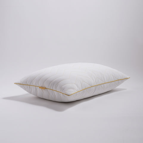 There is a single Simmons Cooling Herringbone Pillow in this image. We have a corner view from a distance. Laying flat on a white background. The pillow has the classic Simmons' yellow lining on the edges, with the yellow Simmons' tag on it. The pillow has a zig-zag herringbone quilt pattern and is covered by an "cool to the touch" nylon cover. 