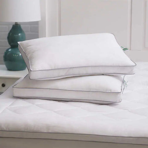 MicronOne Memory Pillow - 2 pack, laying flat on a bed with the bottom pillow laying straight and the pillow on top askew. There are two parallels blue lines on the edges of the white pillows.