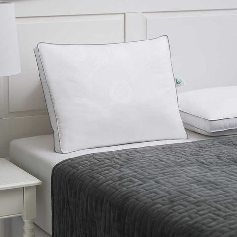 MicronOne Memory Pillow - 2 pack, one pillow standing straight, almost leaning on the headboard behind it and other pillow laying flat beside it almost out of the frame. There are two parallels blue lines on the edges of the white pillows.