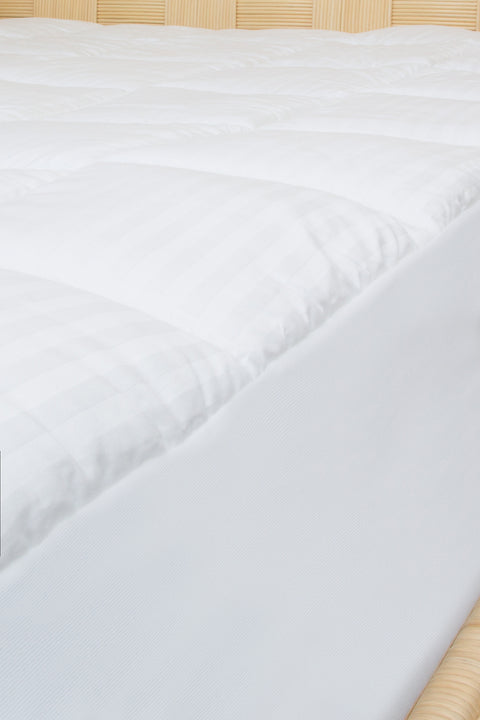Extremely zoomed in image of the side of a bed with 300 thread count cotton, with a  dobby window pane design. The mattress pad is equipped with a stretch skirt that can accommodate mattresses up to 21" in size. 