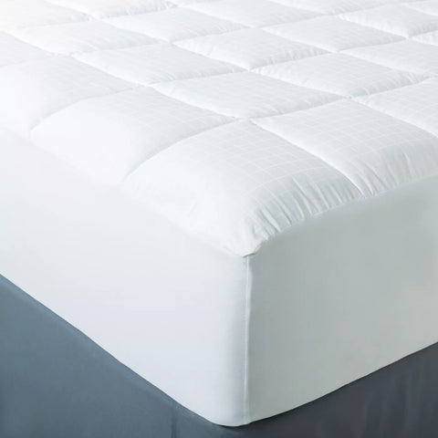 Image of the corner of a bed with 300 thread count cotton, with a  dobby window pane design. The mattress pad is equipped with a stretch skirt that can accommodate mattresses up to 21" in size. 