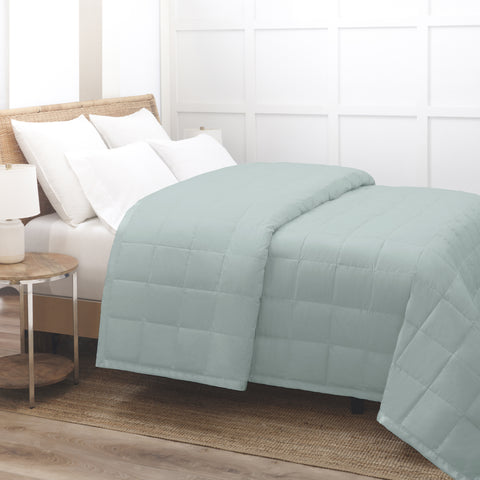 Seafoam Luxury Down Filled Blanket laying perfectly on top of a bed. We are getting a side view of the bed. The blanket is folded over itself at the head of the bed, yet the blanket is still laying pretty flat. The blanket has squares going all across it.