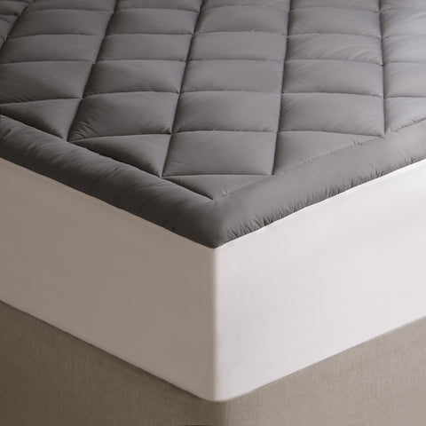 The Graphene Mattress Pad aka the CharcoMattressPad, is shown from the corner of the bed, emphasizing the white edges. With 420 thread count cover fabric. Large diamonds stitching running across the whole surface.