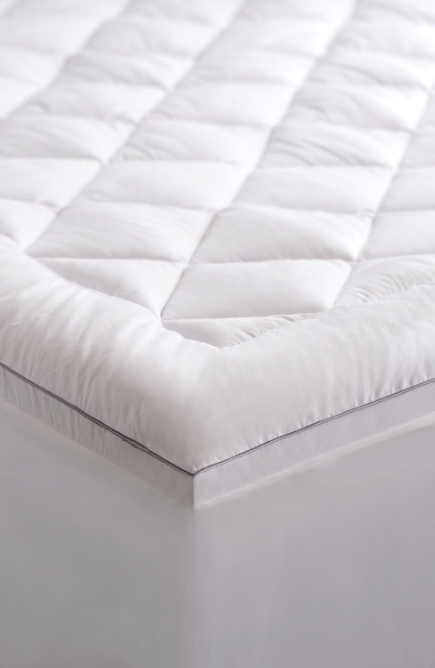 An image of bottom corner of the PureAssure Allergen Barrier Diamond Quilted Mattress Pad. As in the title, there are diamond shapes along the top of the mattress pad. There is a blank border around all the diamonds. The edges of the mattress mad are also plain, no diamond shapes. There is a thin black line dividing the top of the mattress pad and when it curves over the edge.