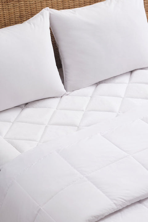 An image of the PureAssure Allergen Barrier Diamond Quilted Mattress Pad. As in the title, there are diamond shapes along the top of the mattress pad. In this photo, it is displaying the mattress pad within a made bed. So there is two pillows at the top and a blanket. However, peaking throw is the mattress pad in all it's glory.
