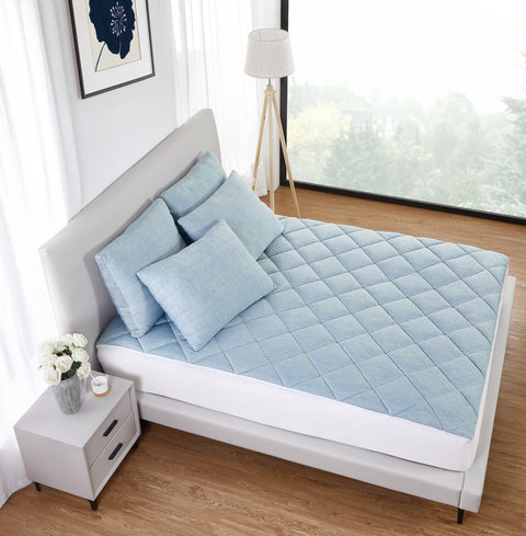 A grey bed frame and head board with the front two black legs of the bed visible. On the bed a four light blue blues, two beside each other with two atop those. The left pillow is askew, leaning on the right pillow a bit. Then there is a light blue mattress pad, with a diamond design,  the sides are white as seen in the front of the image above the base of the bed.
