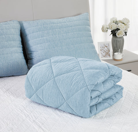 Two light blue pillows beside one another the left one mainly out frame, leaning on a grey headboard. In front of the pillows on a white bed, is a folded up light blue comforter.