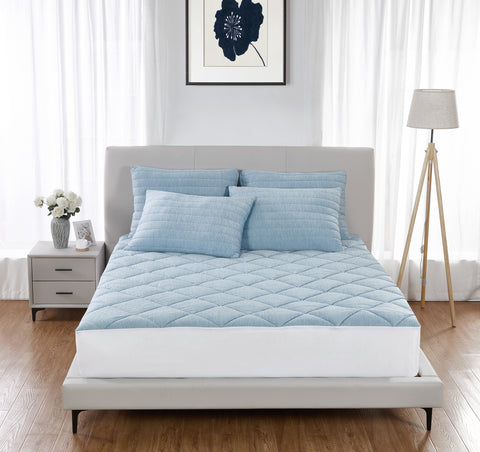 A wooden floor, with a white bedside table on the left with a zebra printed vase holding white flowers. With see through cA bed center frame. Grey bed frame and head board with the front two black legs of the bed visible. On the bed a four light blue blues, two beside each other with two atop those. The left pillow is askew, leaning on the right pillow a bit. Then there is a light blue mattress pad, the sides are white as seen in the front of the image above the base of the bed curtains.