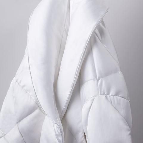 A zoomed in image of the top part of the plush Satin Puffer Robe being displayed here on a white background. Diamond shaped stitching across the whole thing. Hoodless. White elegant, hotel styled robe.