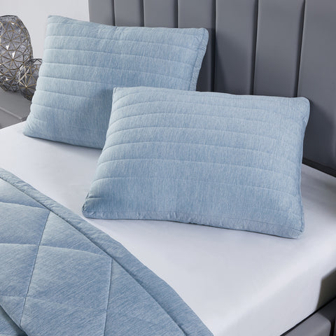 Two light blue pillows, the one on the left is slightly tucked beneath the one on the right. The pillow o nthe right is leaning onto the pillow on the left at an angle.