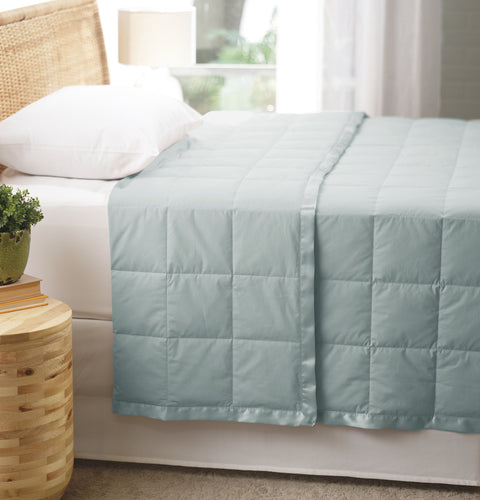 Seafoam Luxury Down Filled Blanket laying perfectly on top of a bed. We are getting a side view of the bed. The blanket is folded over itself at the head of the bed, yet the blanket is still laying pretty flat. The blanket has squares going all across it.