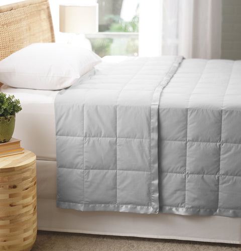 Silver Luxury Down Filled Blanket laying perfectly on top of a bed. We are getting a side view of the bed. The blanket is folded over itself at the head of the bed, yet the blanket is still laying pretty flat. The blanket has squares going all across it.