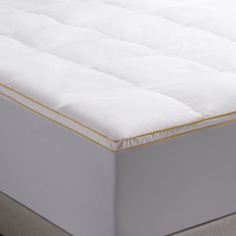 Poly Prime Feather Fiber Fill Bed displayed on a bed. The zoomed in photo show the corner of the bed emphasizing the classic Simmons's yellow stitching.