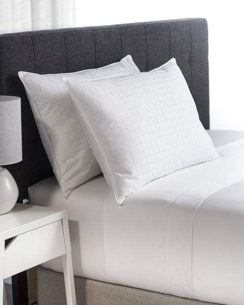 Plush Perfect Gel Fiber Pillow (Overstuffed) (Set of 2) both pictured. One leaning on a dark grey headboard while the other is leaning on that pillow.
