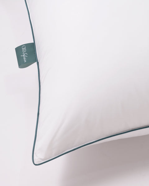 CBD Pillow Protector with 233 thread count 100% cotton pillow. protector. Photo taken from above. Only focusing on the left corner of the pillow, emphasizing the blue stitching around the pillow as well as the tag sticking out.