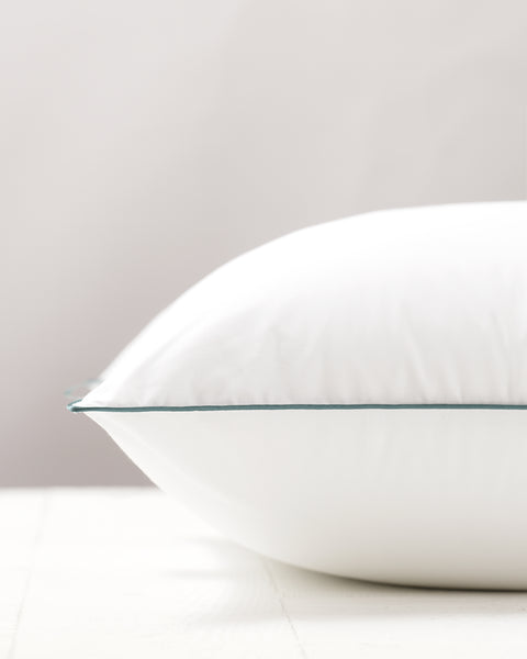 Image of a pillow laying flat and plump, only revealing the top half of the pillow. Side view, P.O.V. from the longer side. A solid blue stitching across the center. CBD Pillow Protector with 233 thread count 100% cotton pillow. protector