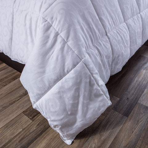 One DownLinens 300 Thread Count Down Alternative Comforter with square stitching all across the entirety of the comforter. Zoomed in to the bottom corner of the bed where the blanket is hanging over and allows you to see the swirl details on the entire comforter.