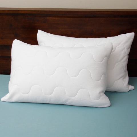 Two pillows leaning on a brown headboard and a blue bedsheet. The pillows re white and have three parallels lines, the lines make several concaves, alternating up and down.