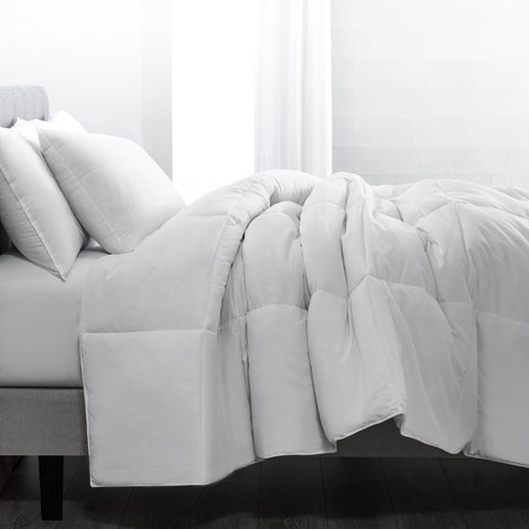 Classic Peachy Down Alternative Twin Comforter. Despite the name "peachy" the color of the blanket is in fact white. Side view of a bed. Large blanket laying atop a bed. Crumpled up as if someone had slept in the bed and threw the covers to semi make the bed. With large square stitching across the whole thing. 
