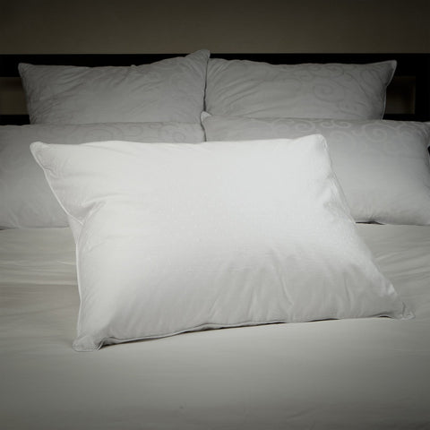 A bed with two pillows leaning on a headboard,. Two more pillows in front of those pillows. Then front and center in front of those four pillows, is a single Perfect White Goose Down Pillow - 50/50 Fill - Medium Plush Support.