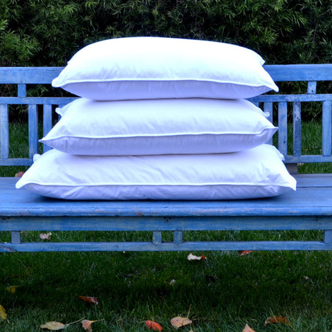 3 white, 180 thread count poly/cotton blend plush pillows stacked onto each other on a blue park bench