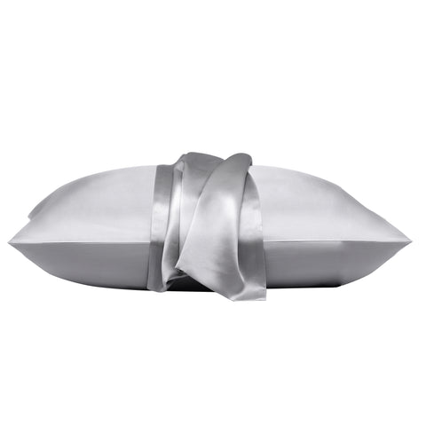 On a white background is a pillow laying flat. The pillow is in the gray silk pillow case, with another gray pillow case on the center of the pillow, overlapping on itself.