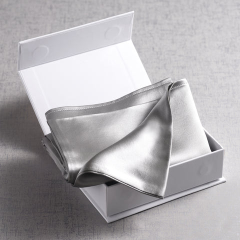 In a small little white box, that is open, is a folded up gray silk pillow case.