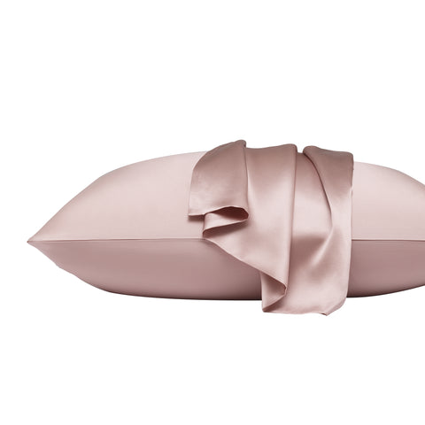 On a white background is a pillow laying flat. The pillow is in the pink silk pillow case, with another pink pillow case on the center of the pillow, overlapping on itself.