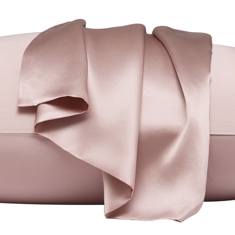 On a white background is a pillow laying flat. The pillow is in the pink silk pillow case, with another pink pillow case on the center of the pillow, overlapping on itself. This image is almost trying to emphasize the pillowcase that's resting on top, by zooming in.