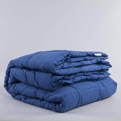 Nautical Blue Peachy Down Alternative Comforter folded up and you can see that there is square stitching running up and down the blanket. There is a tiny white tag with blue letters that spell "Downlinens" sticking out of the blanket as well.